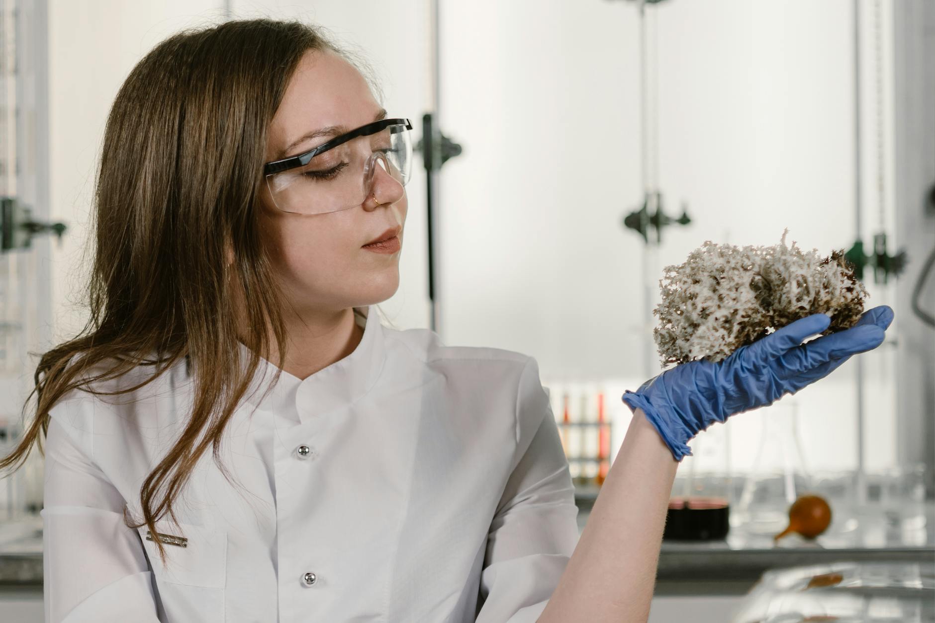 Female scientist in lab coat and goggles analyzing a biological sample.