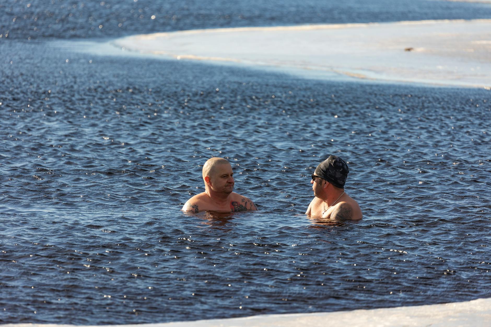 Two men enjoying winter swimming in icy waters, showcasing extreme cold exposure.