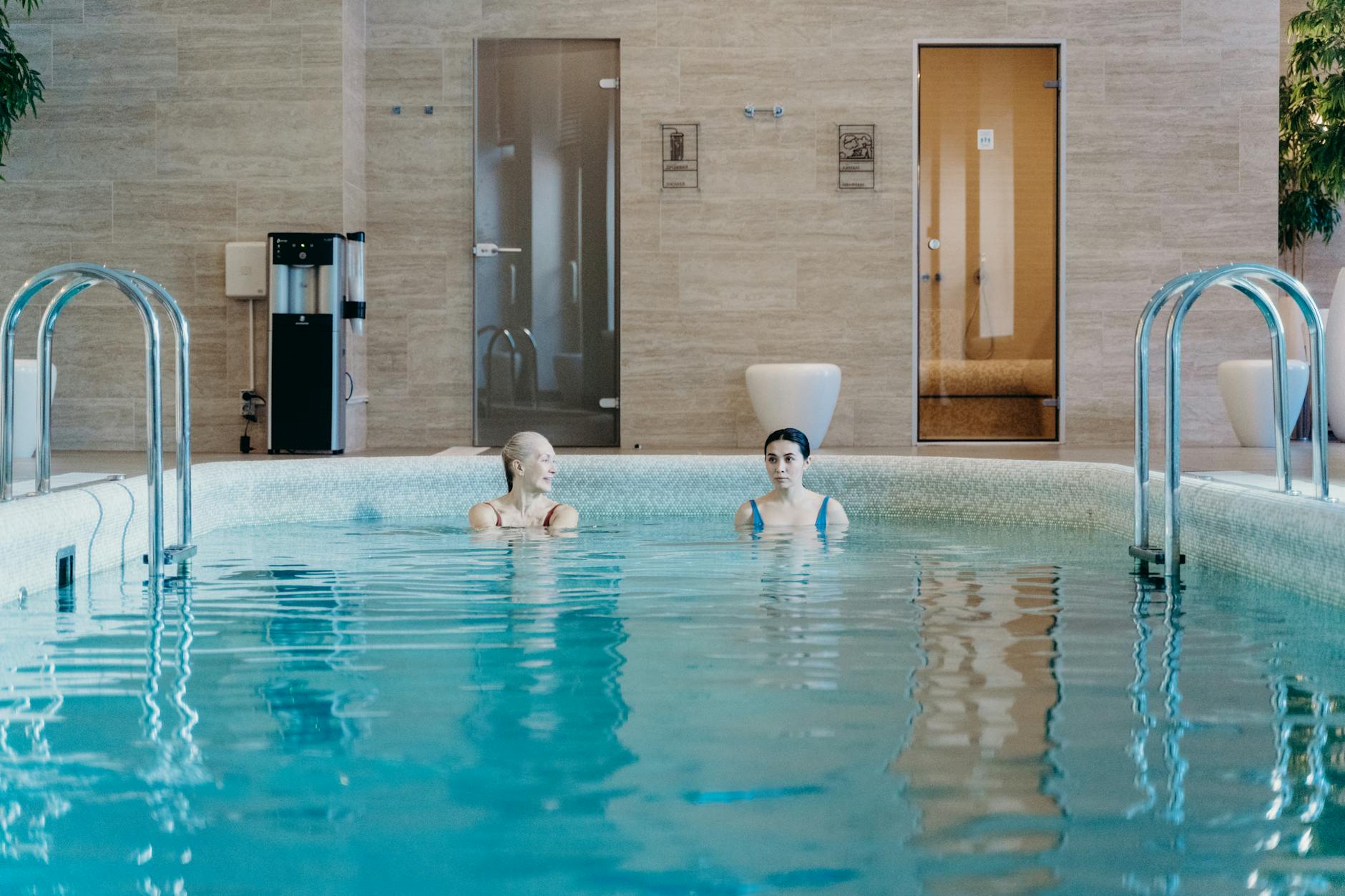 Two women enjoying a leisurely swim in an indoor pool, capturing relaxation and tranquility.