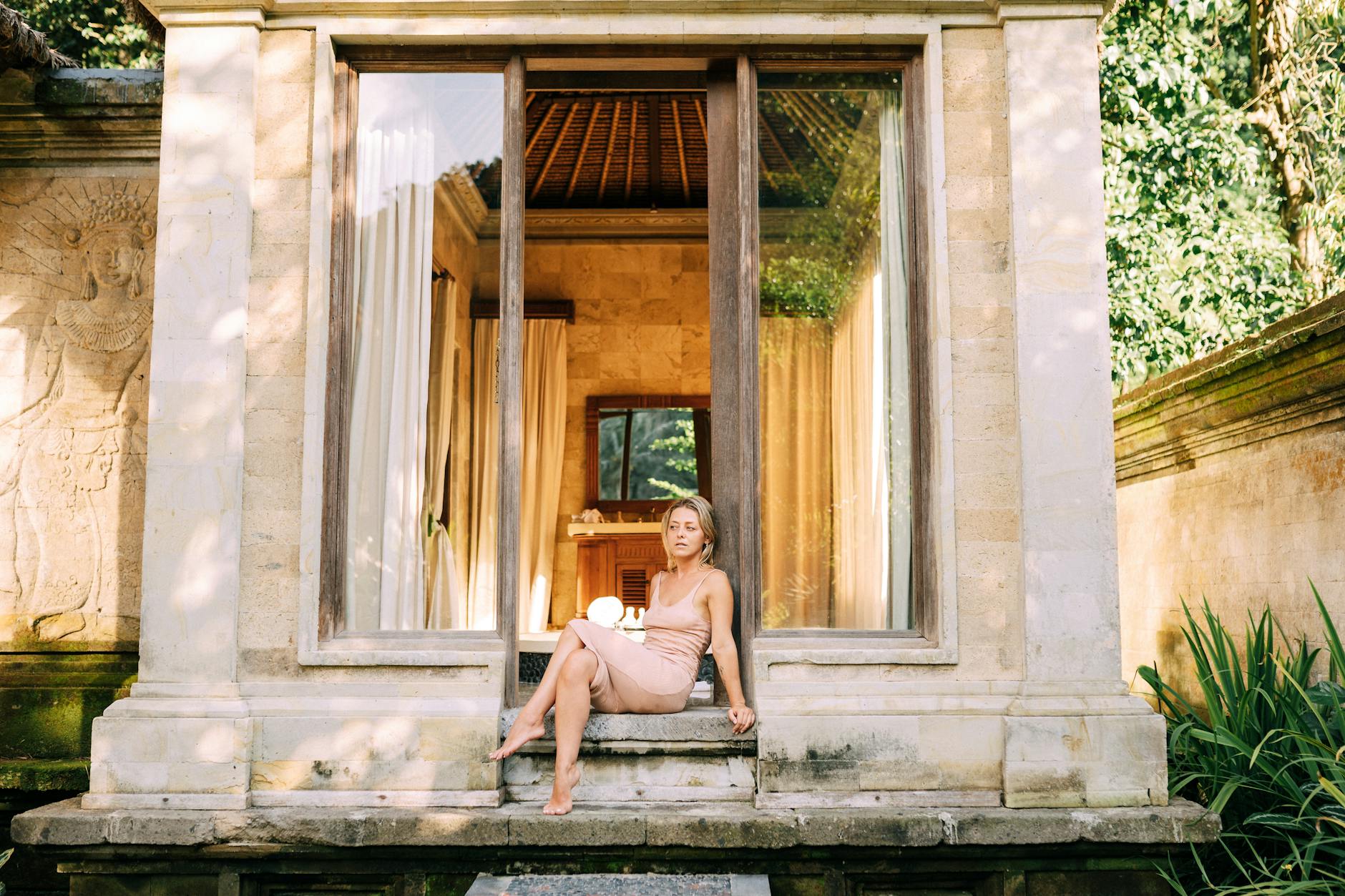 A woman in an elegant dress sits gracefully by a luxurious villa entrance, highlighting summer relaxation.