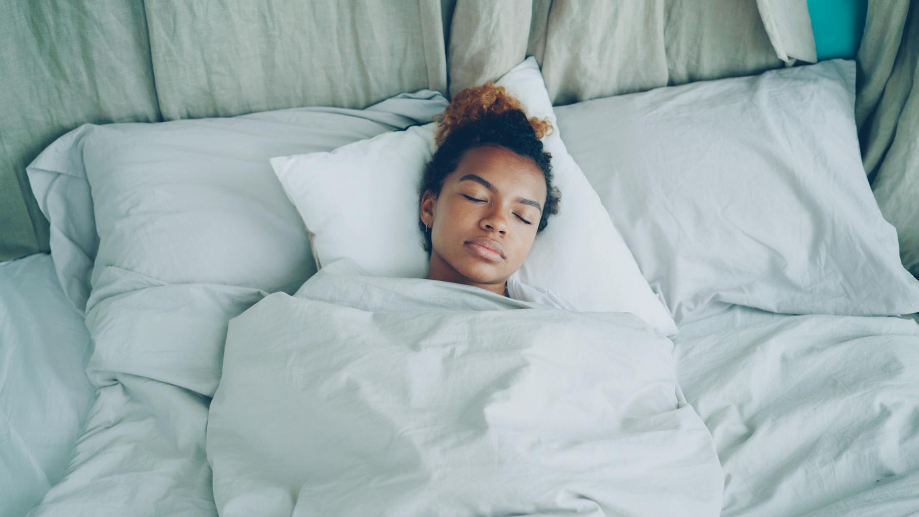 A serene woman peacefully sleeping in a cozy, white-sheeted bed.