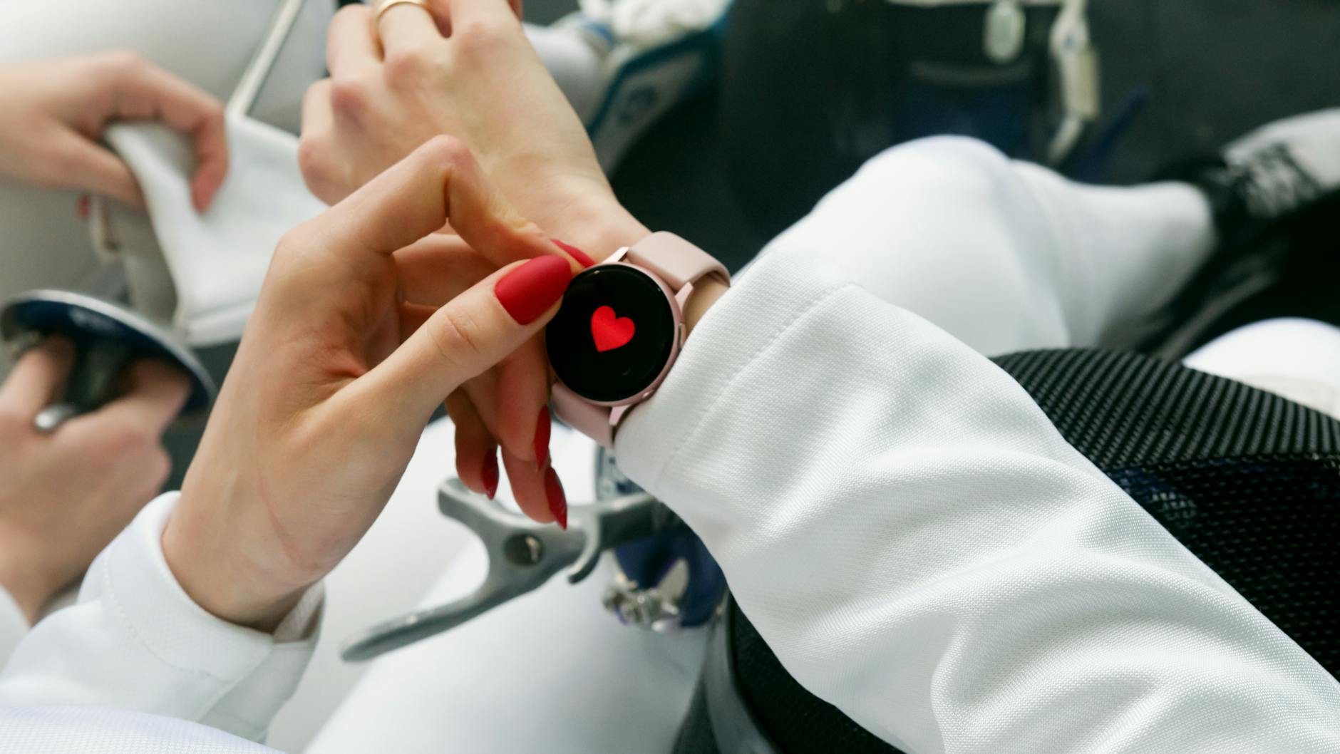 Close-up of a woman's hand with red nails interacting with a smartwatch displaying a heart icon.