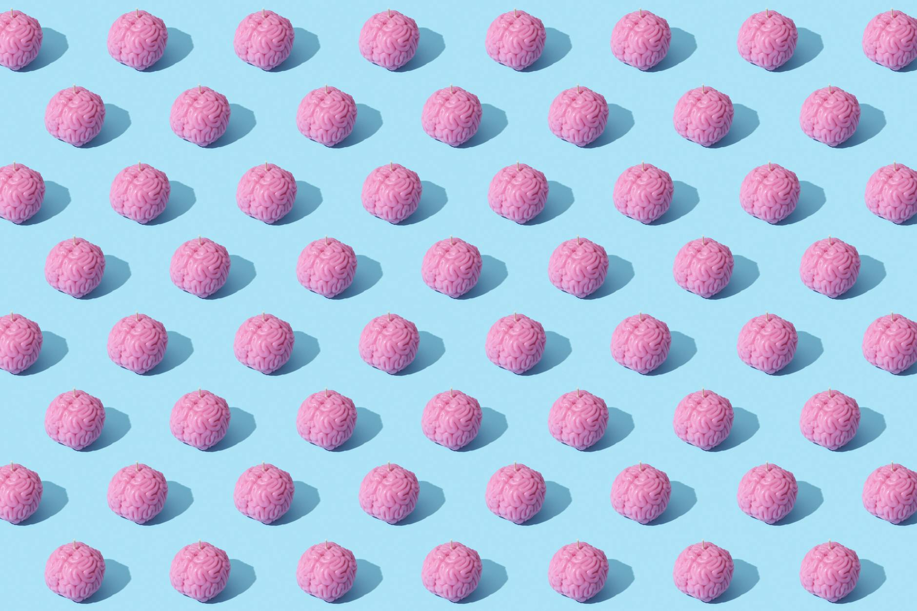Creative composition of pink brain models in a repeating pattern on a light blue surface, showcasing abstract thinking.